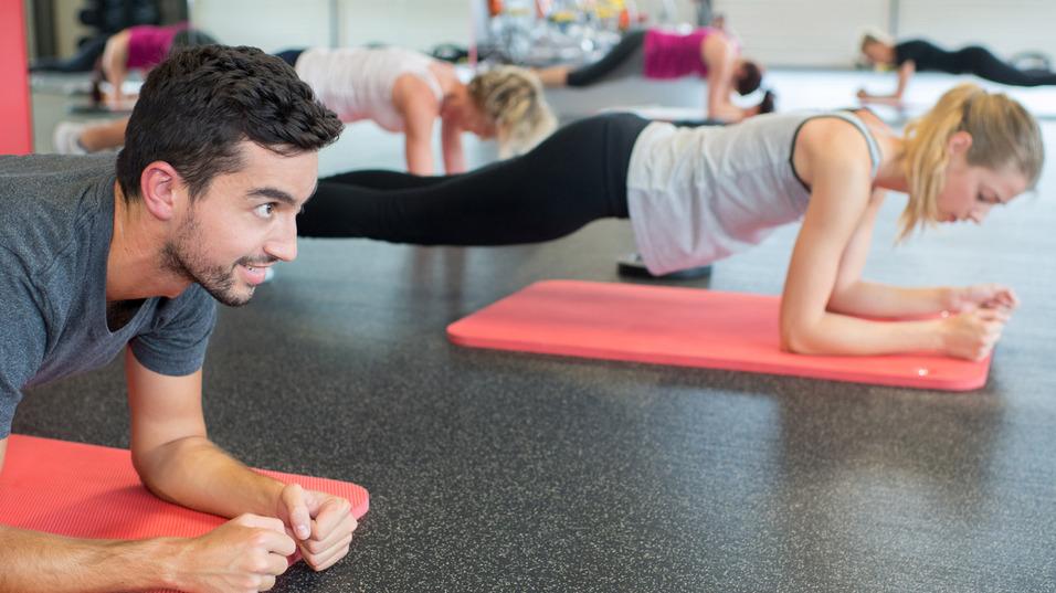 Mann und Frauen machen Plank-Übungen auf Yogamatten in einem Fitnessstudio. Helle, sportliche Atmosphäre.